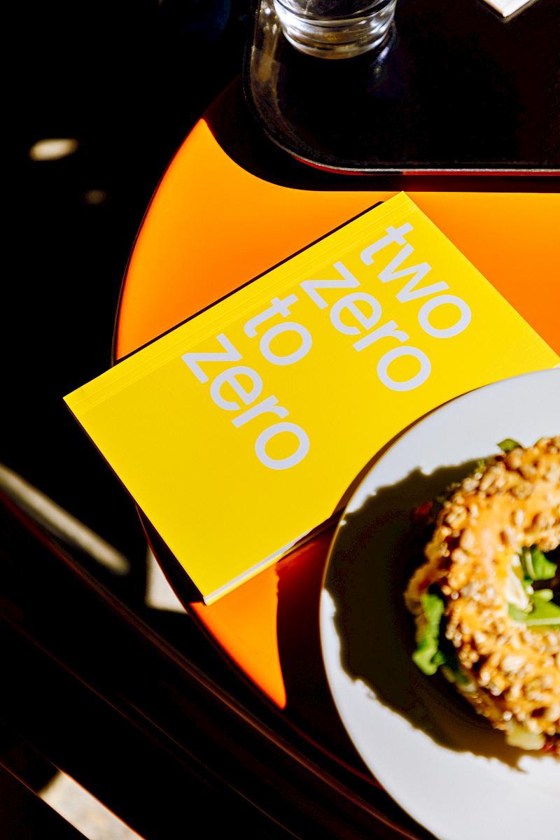 A yellow planner lying on an orange table near a bagel